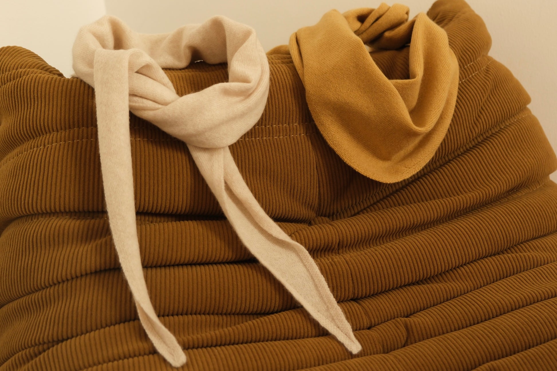 Finding Dodo Kaschmir-Dreiecktücher in Mustard und Pearl dekorativ drapiert auf einer braunen modischen Couch.