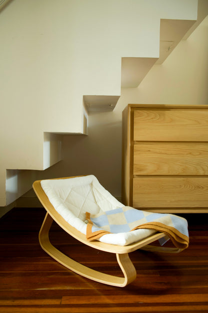 Beige-braune Finding Dodo Kaschmirdecke Ari gefaltet auf einem Stuhl in einem modischen Wohnzimmer vor Treppe und Kommode.