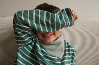 Kleiner Junge im gestreiften Pullover trägt das salbeigrüne Finding Dodo Kaschmir-Dreiecktuch und verdeckt spielerisch sein Gesicht.