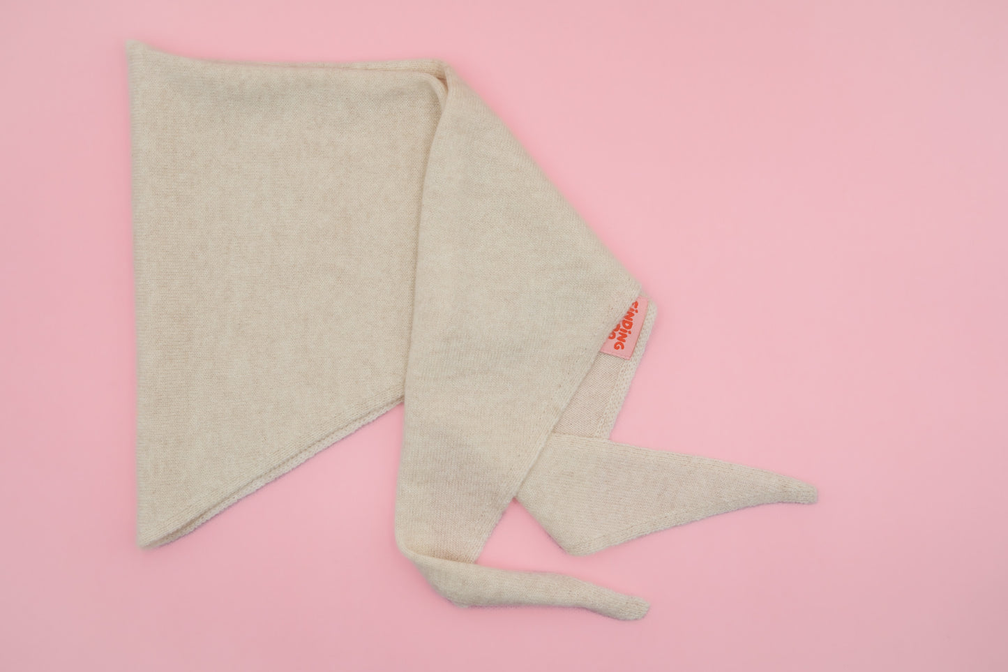Beiges Finding Dodo Dreiecktuch aus 100% Kaschmir in der Farbe Pearl auf rosa Hintergrund.