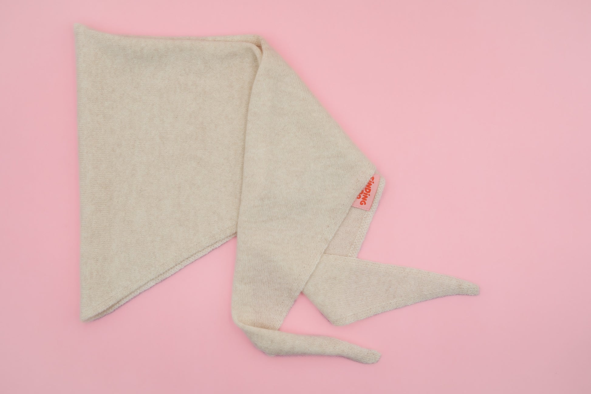 Beiges Finding Dodo Dreiecktuch aus 100% Kaschmir in der Farbe Pearl auf rosa Hintergrund.