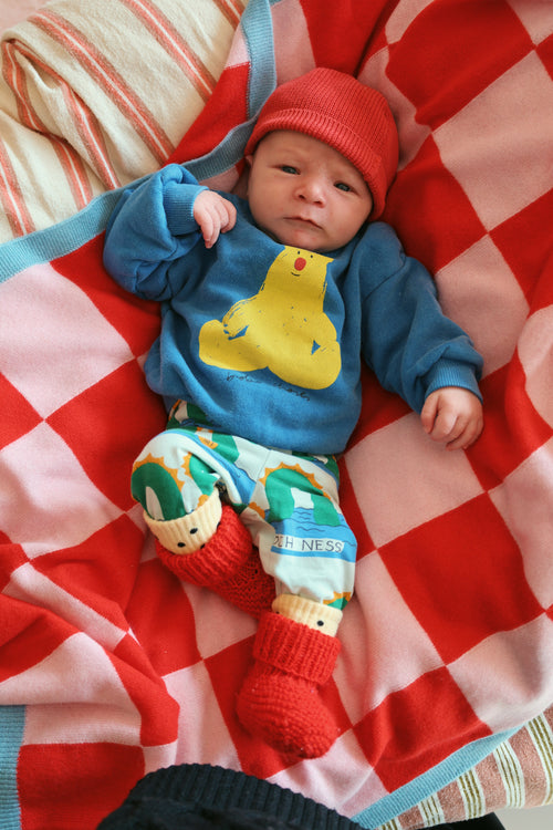 Baby in bunten Kleidern mit roter Beanie auf der Finding Dodo Alma Kaschmirdecke in Blau-Beige.